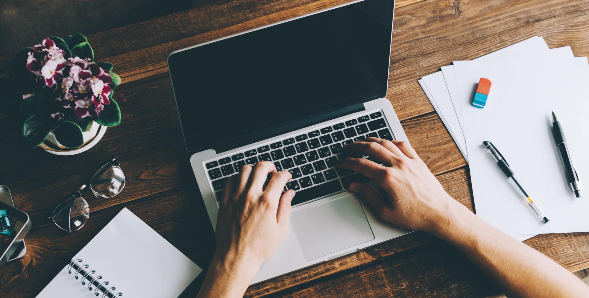Someone blogging at a desk on a silver laptop.